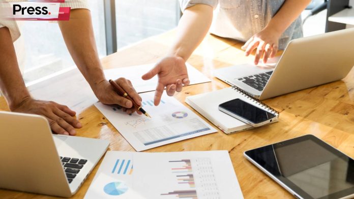 A group of 3 men around a table full of documents, discussing charts and different types of SEO, from on-page to off-page to technical