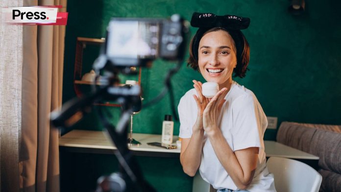 A woman engaged in content creation, sitting in front of a camera and smiling, with her hair tied up in a fancy way.